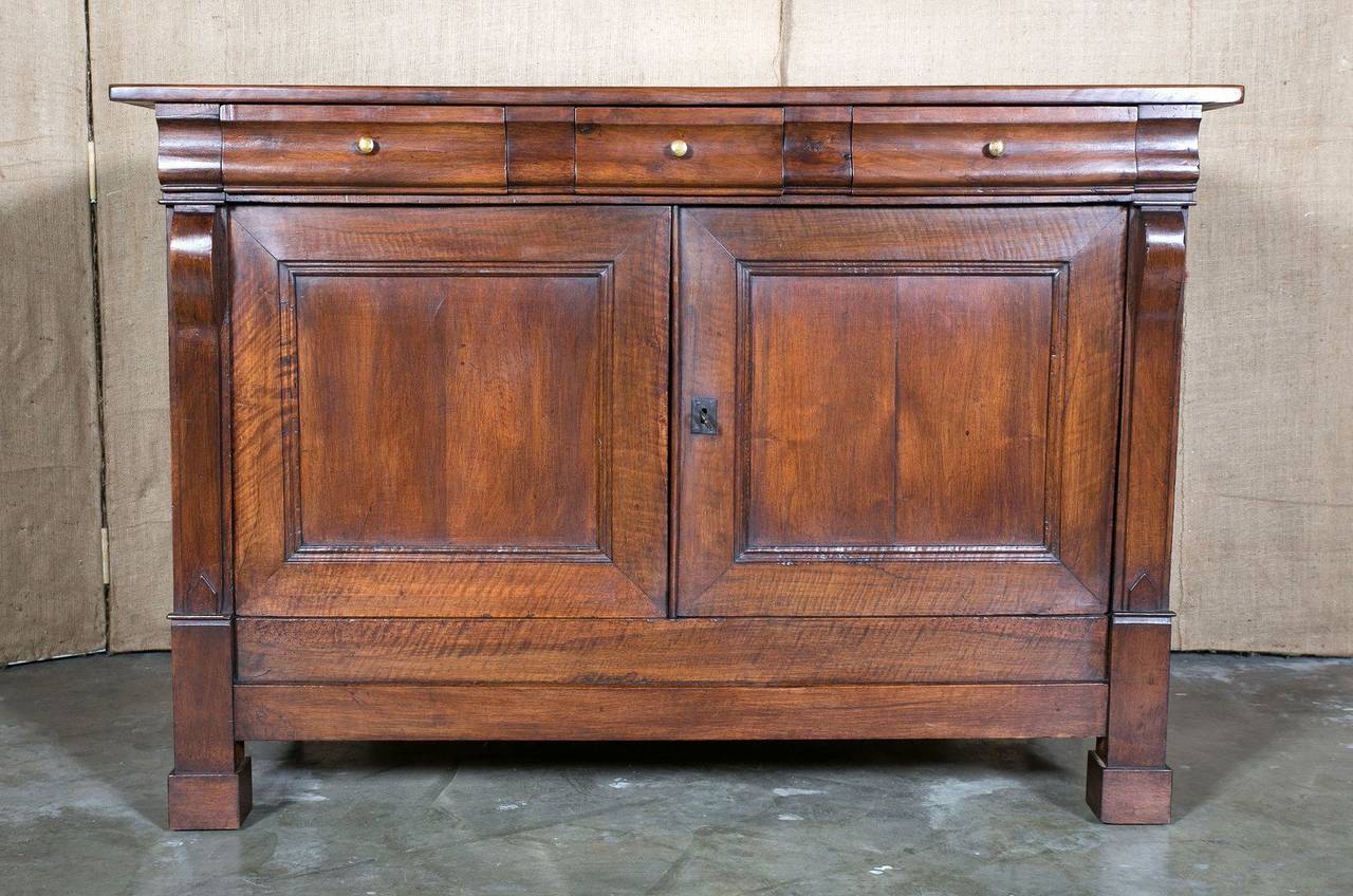 Handsome French Restauration period buffet in walnut. Three drawers above two doors flanked by scrolling pilasters. Raised on bracket feet. The clean lines and elegant curves of this piece make it highly desirable for today’s modern interiors.
