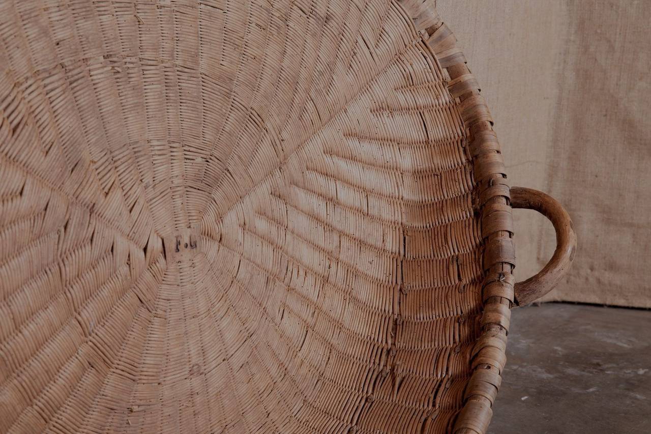 Charming antique French winnowing basket with wooden handles and initials FG. Originally used to separate the wheat from the chaff. Peasant farmers would hold the flat side of the basket against their body and toss the wheat into the air. The chaff