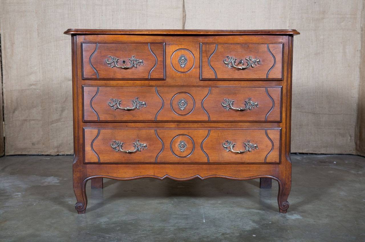 Charming Country French Louis XV style walnut commode with serpentine front, four carved drawers, bronze hardware and paneled sides. Shaped apron resting on short cabriole legs ending in scrolled French toes on pegs.