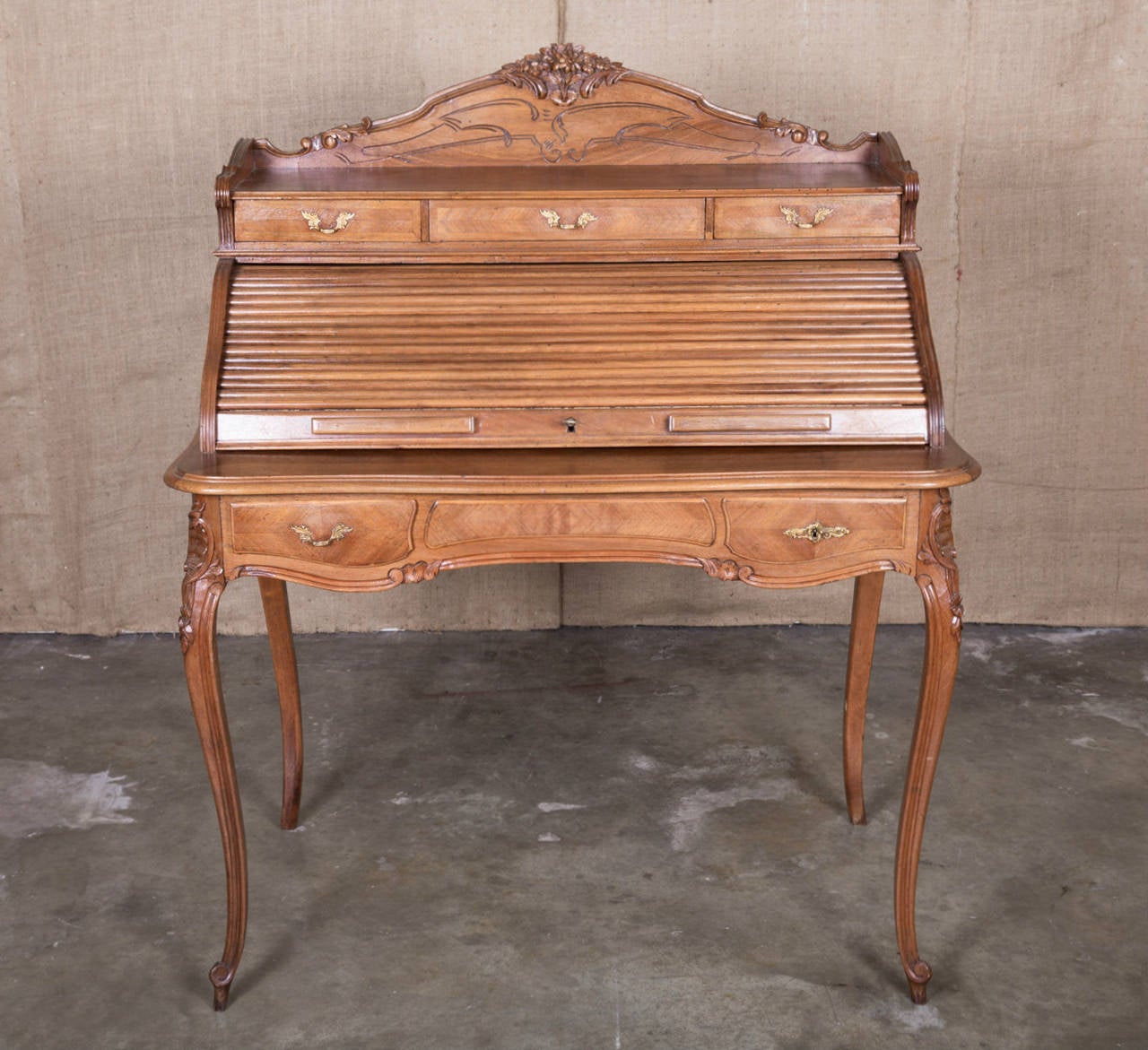 Charming Country French Louis XV style ladies tambour roll top desk or bureau à cylindre of walnut and marquetry with carved floral and foliate backsplash and three upper drawers. Interior with two shelves and storage room, the writing surface is