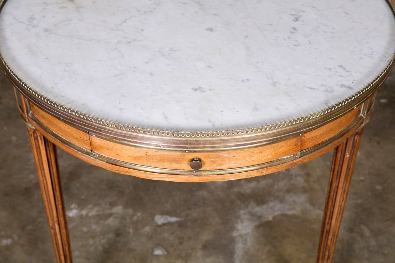 Handsome Louis XVI style bouillotte side table in walnut with a Carrara marble top surrounded by a pierced brass gallery. The apron has brass trim and a drawer for cards and chips and a slide with embossed leather top that was originally used to