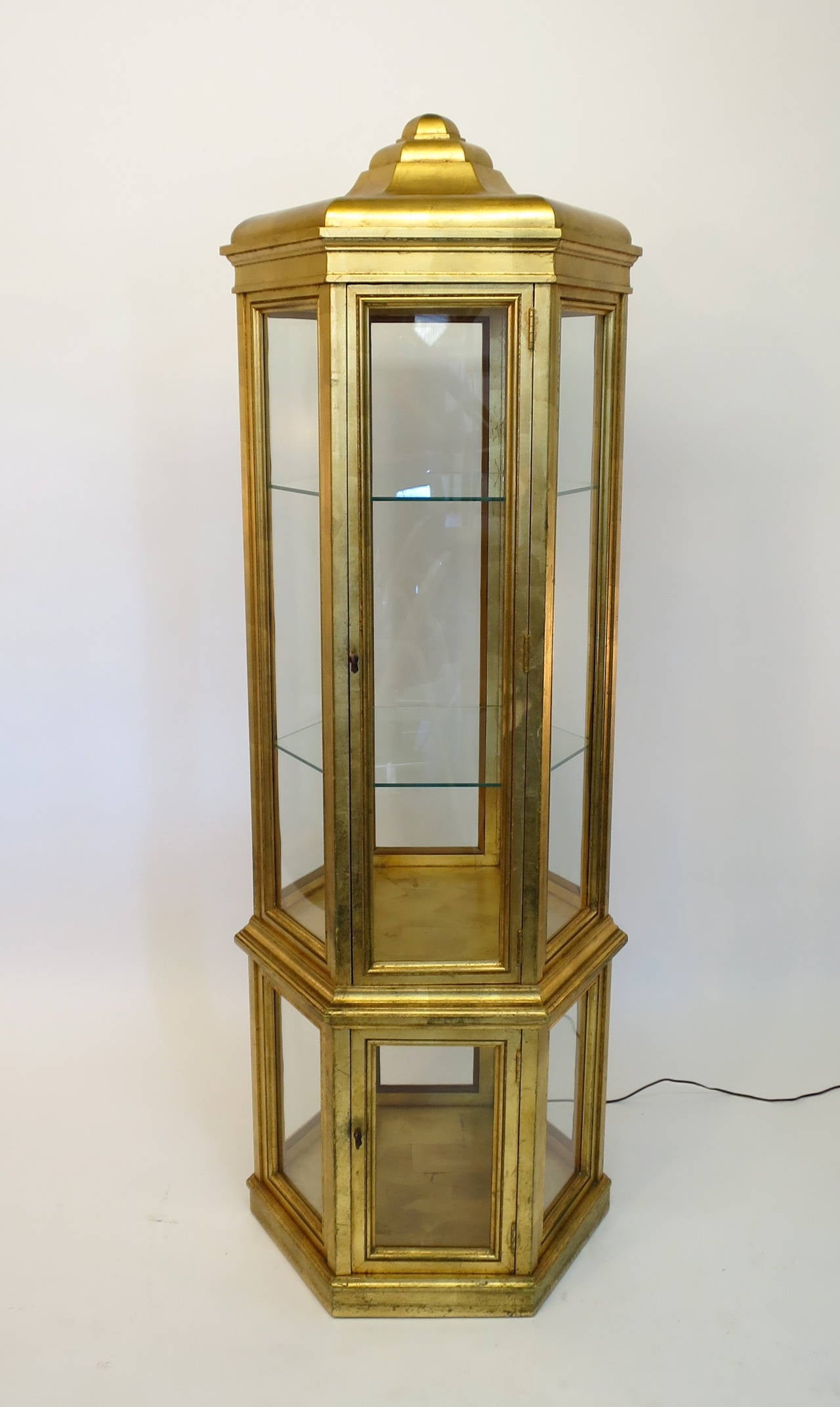 Beautiful gold leaf curio cabinet or vitrine manufactured by Weiman Furniture Company. Upper and lower storage with build-in lighting. Gold leaf on interior and all exterior sides. Features two doors and two glass shelves. Very nice original