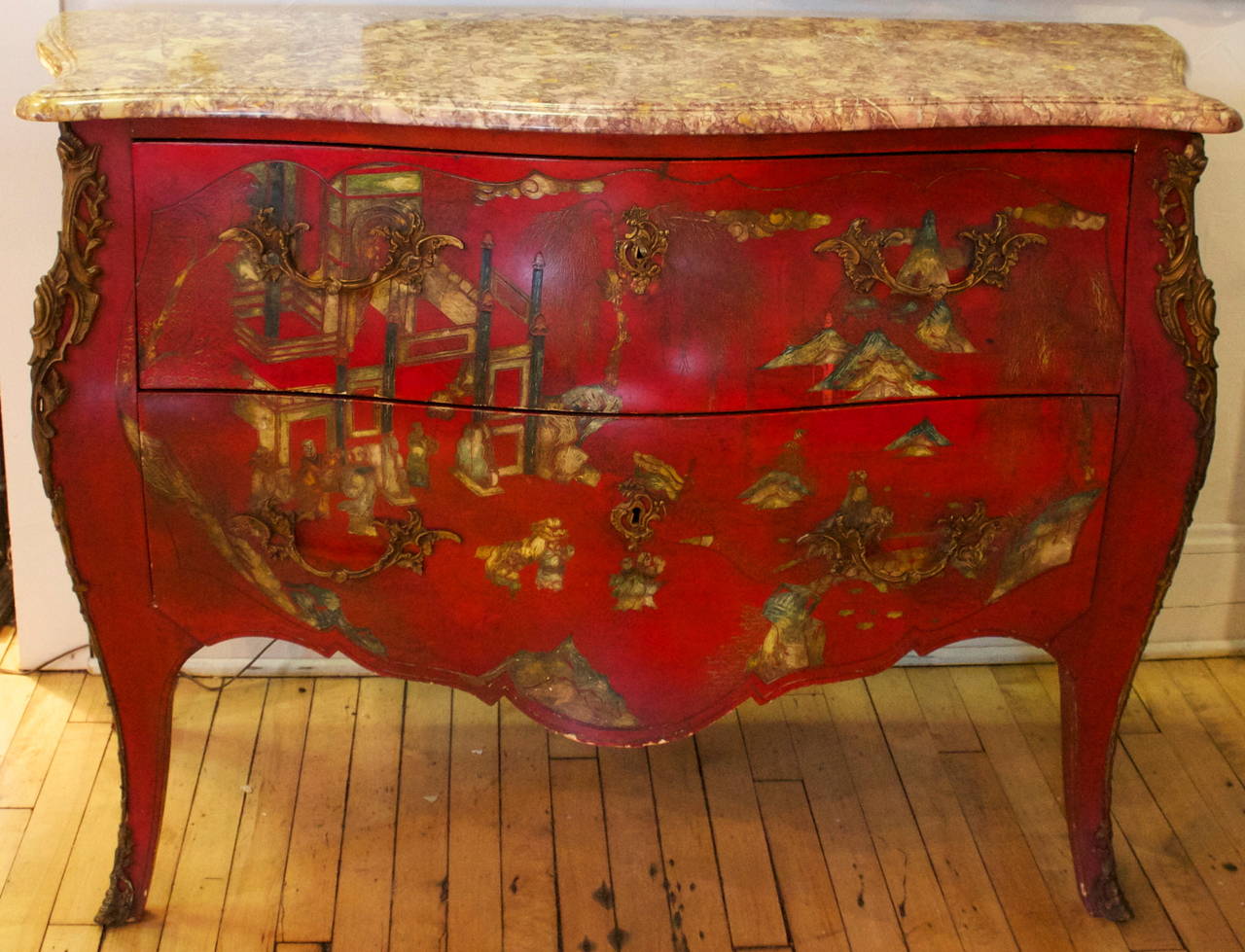 The breche violette marble-top over a conforming case with two long drawers raised on cabriole legs, decorated with a scene of pavilions and figures in a landscape on a red ground.