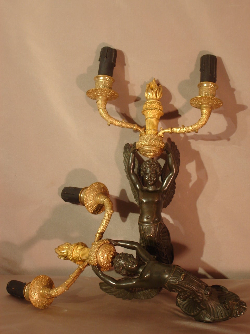 Pair of winged children sconces supporting two lighted arms in patinated bronze and chiseled and gilded bronze. These fixtures are ending in the lower part by bouquets of acanthus leaves in matte bronze patina.

The upper part is decorated with