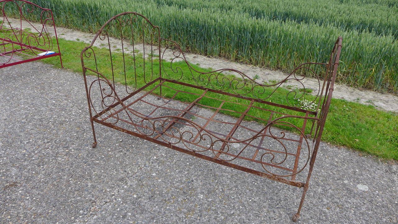 French hand forged iron bed with scrolling design and raised on castors.