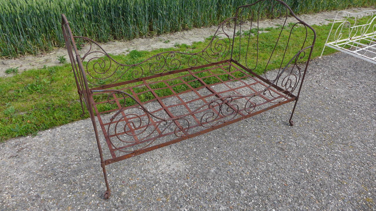 A French hand forged iron bed with scrolling design and raised on castors.