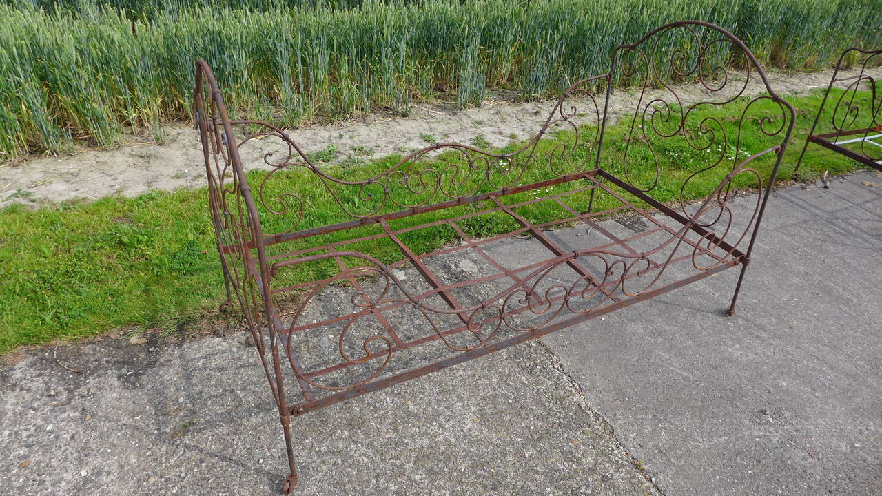 A French hand forged iron bed with scrolling design and raised on castors.