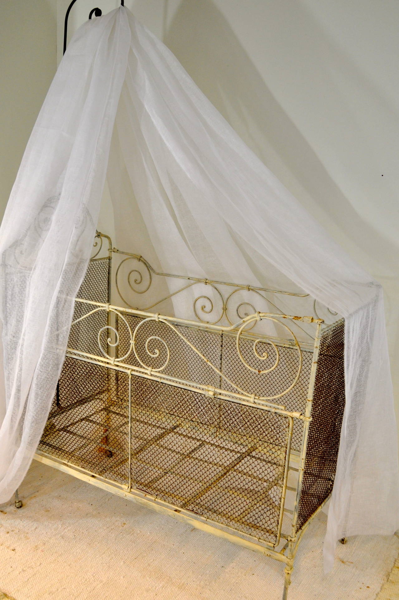 A very beautiful and elaborate French folding baby bed is made in a combination of wrought iron with scrolling design and wire netting. Both sides can be folded, if needed and as you like it. The bed is raised on castors and the sky is made from