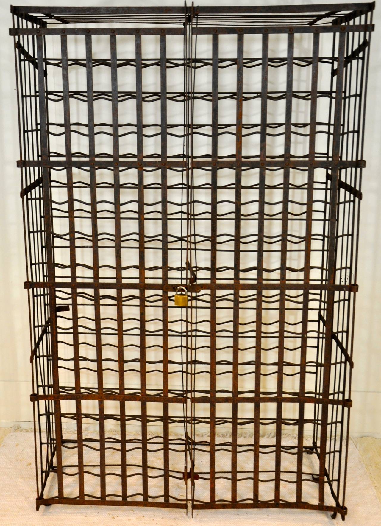 A French iron wine cage who can store 300 bottles in a double row and who is lockable with a pair of hinged doors. There are flanges to the rear so that it may be fastened to the wall for a greater stability.