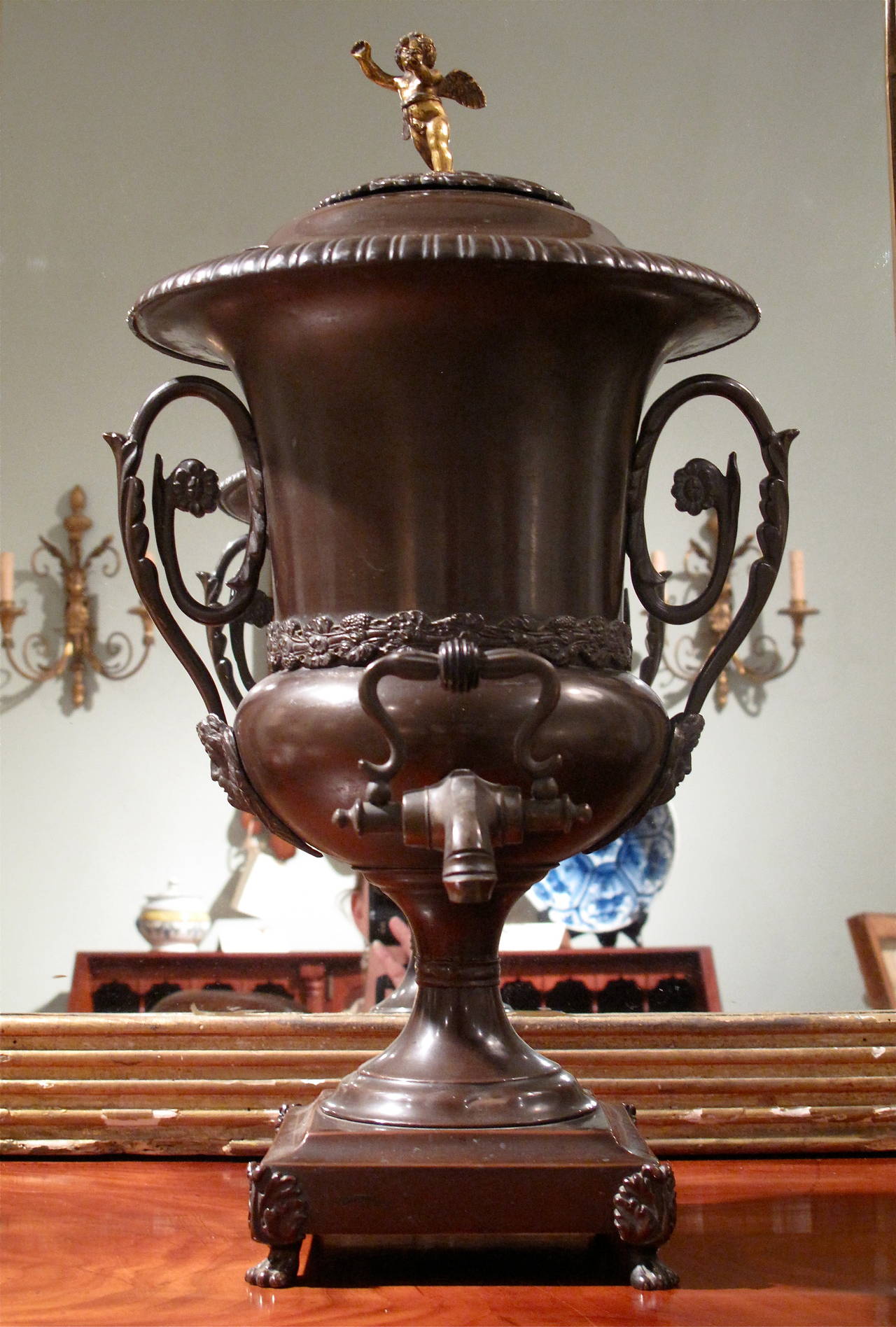 A very fine ca. 1810 footed hot water urn of patinated copper, with wonderful sculptural details. A gilded putto serves as the handle for the two part lid.