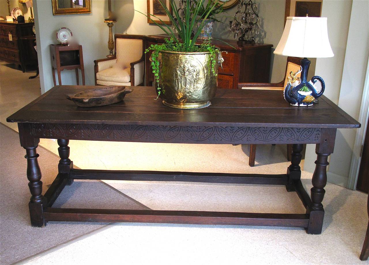 A late 17th century English oak stretcher base table with a breadboard ended plank top. Baluster legs support the apron of the table, the apron decorated with compass drawn incised carving.