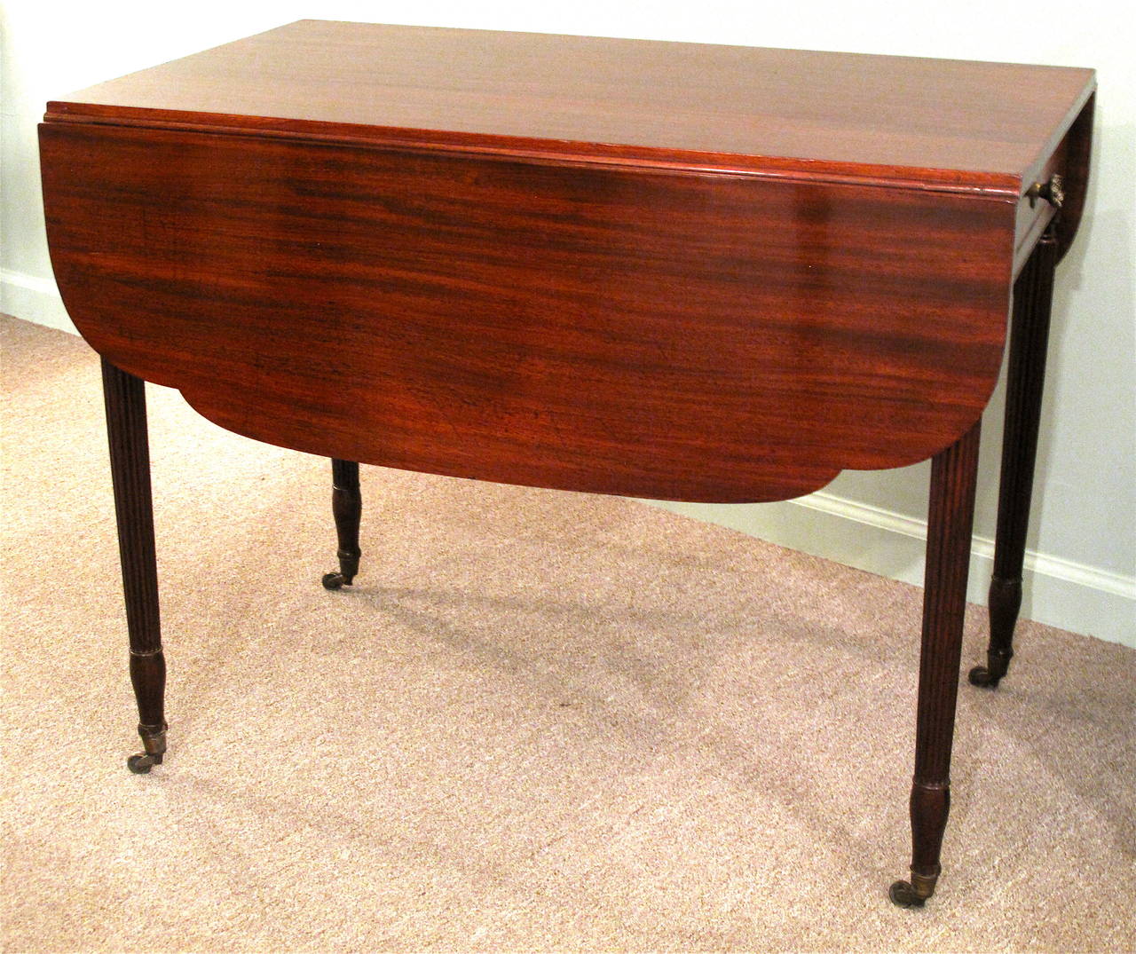 A fine mahogany pembroke table, with shaped leaves and the slender reeded Sheraton legs ending in casters that are characteristic of New York in the very early 19th century. Each apron end has arched inlay of flame mahogany over the legs. Original