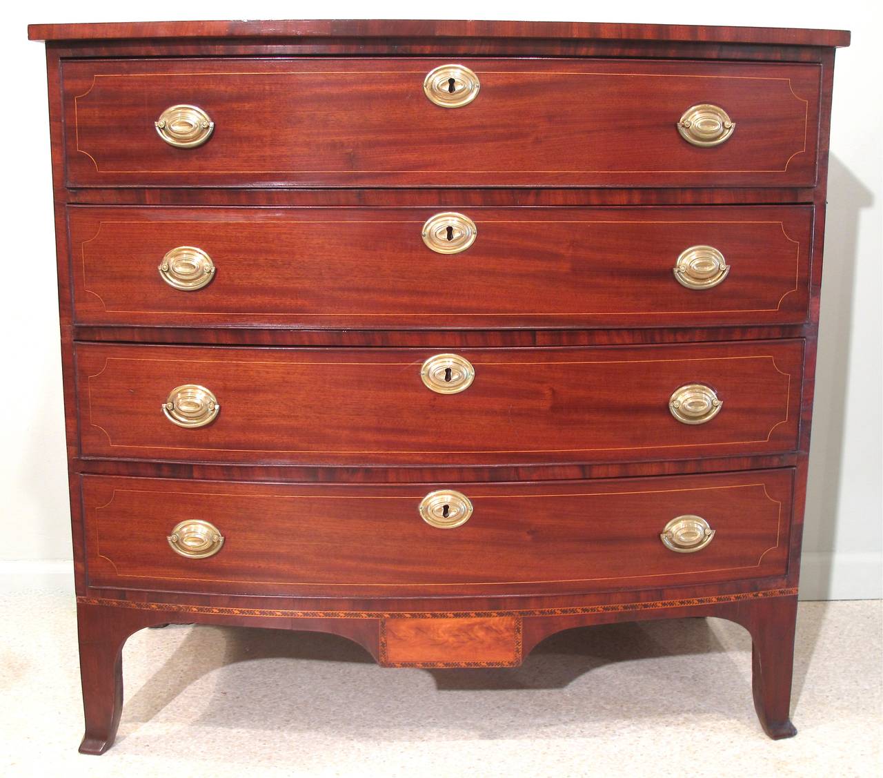 An elegant bow front four drawer chest, ca. 1800-1810 on tall French feet and with the dropped panel apron and flame birch inset and detailed inlaid banding typical of Portsmouth, NH. Drawer fronts are mahogany with satinwood string inlay. Top and