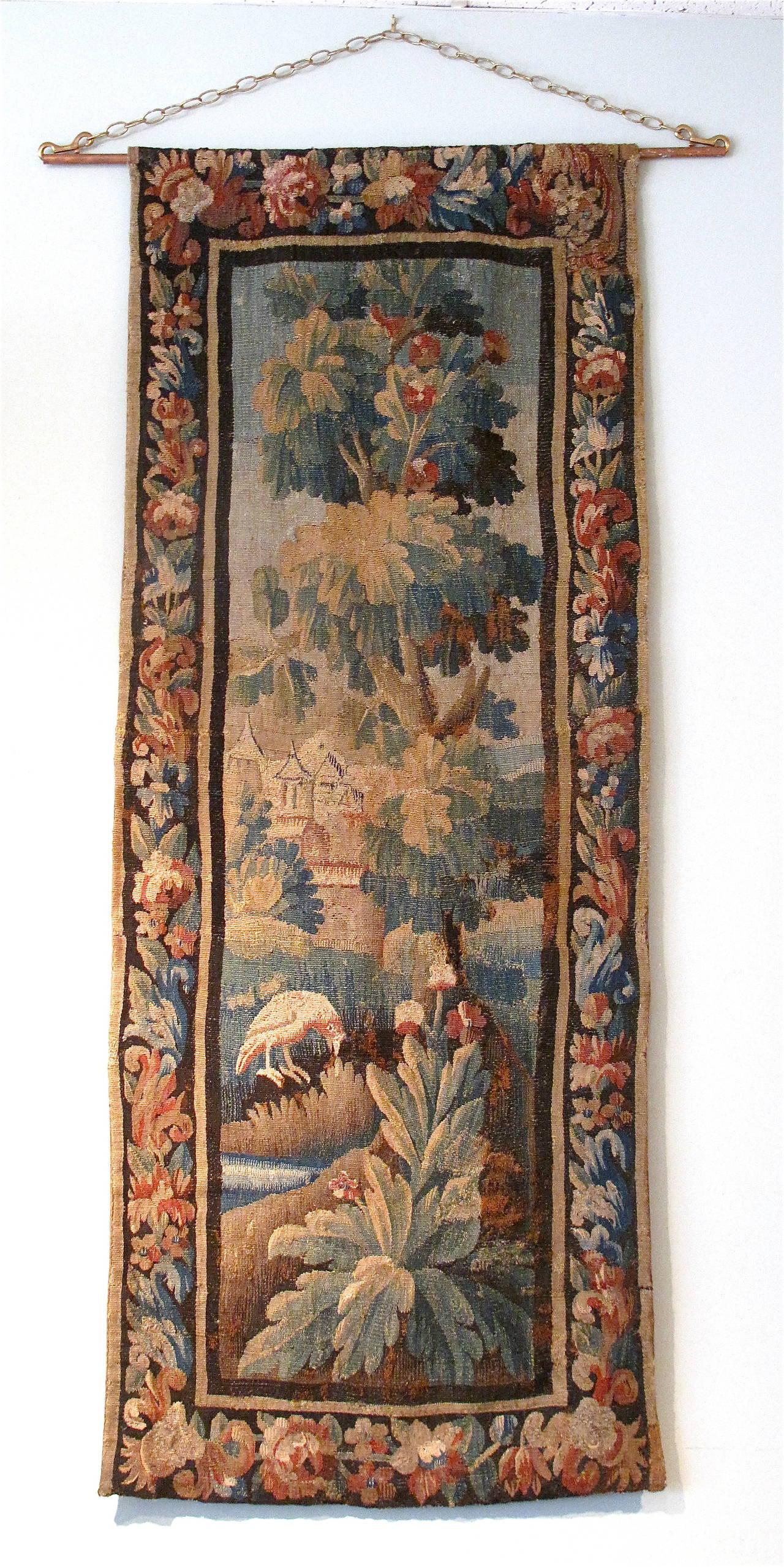A scenic landscape tapestry featuring a distant castle amid boldly depicted trees and foliage, with a bird in the foreground. The original borders encircle the scene. Rustic and charming aspect to the whole.
