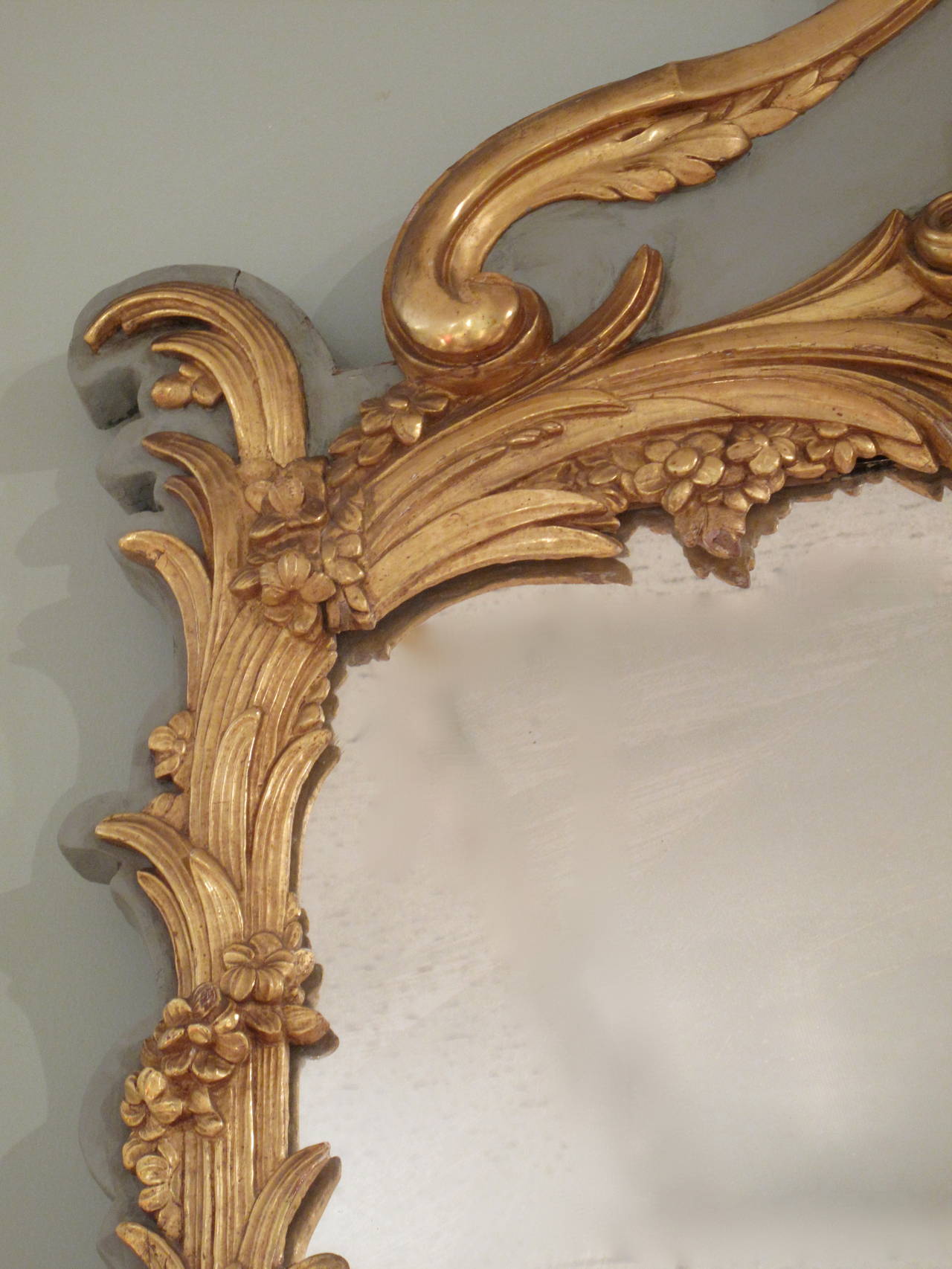 An elegant carved giltwood on grey ground crested mirror, late 19th century, the sides comprised of gathered palm fronds encircled by delicate floral garlands. The palm fronds spring from Rococo shell and leaf ornament at the base of the mirror and