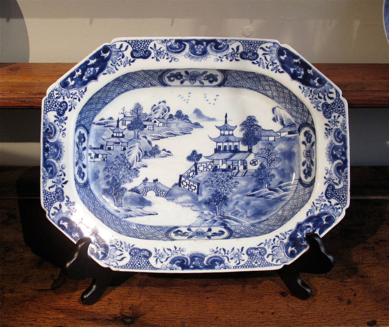 An early 19th century (ca. 1800-1820) blue and white serving dish with shaped edges decorated with a flower and reserve border over a diaper pattern recess surrounding a traditional detailed Nanking tea house scene.