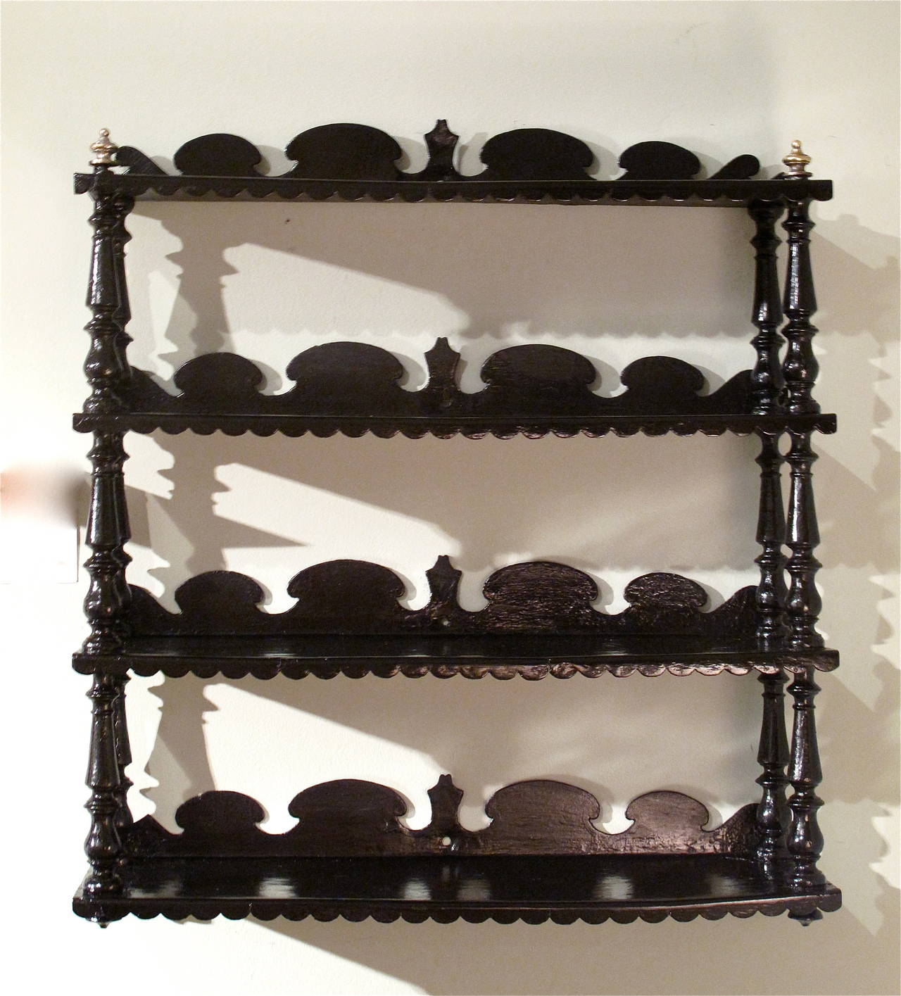 A charming 19th century hanging shelf, probably English, but possibly American, dating ca. 1830-1850, with turned elements supporting the four levels of scalloped and shaped tôle shelves, the top shelf finished with two brass finials.