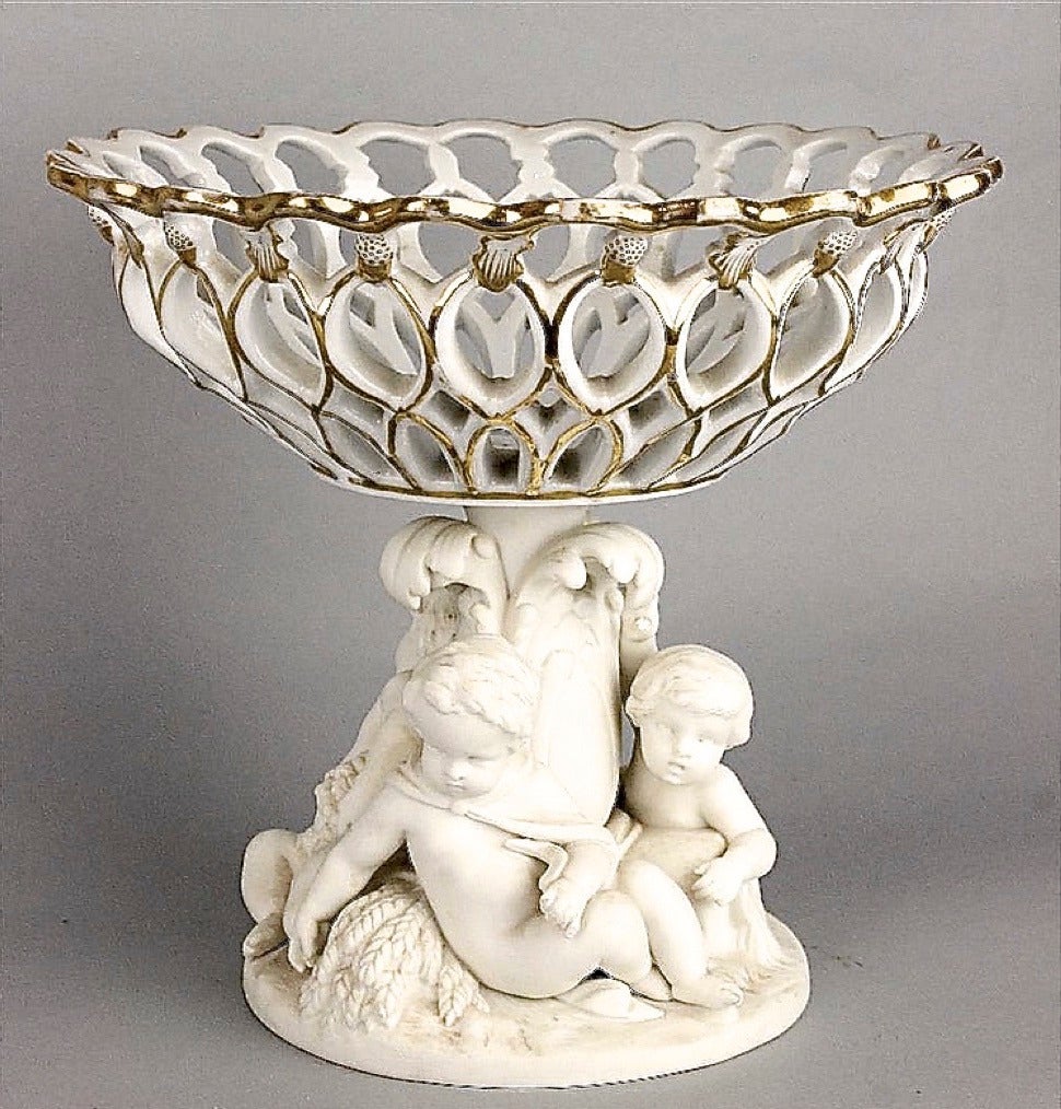 Minton Compote with Pierced Basket
A very fine Minton compote with a Parianware pedestal base of frolicking putti supporting a glazed and parcel gilt basket. Stamped Minton and date marked 1865 on the bottom.