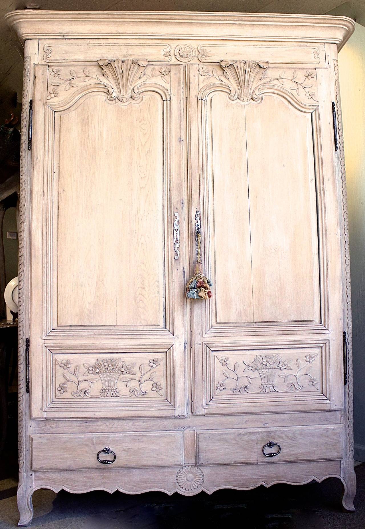 A handsome armoire with a subtle finish of stripped and transparently white washed oak. Crisply carved symmetrical door panels are set off by bold acanthus crests and floral sprays. The curved corners are also nicely detailed with guilloche pattern