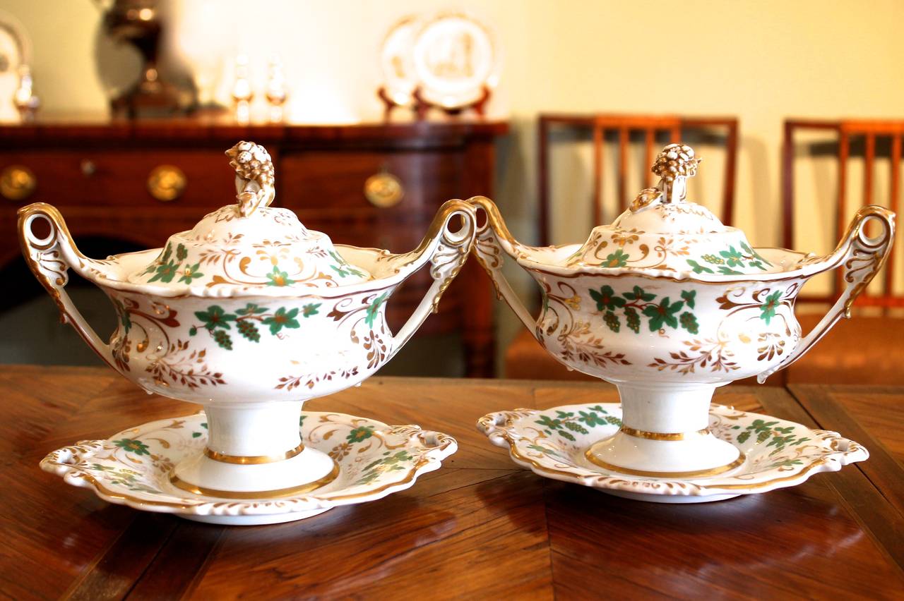 A fine pair of green and gilt footed sauce dishes on fixed underplates, ca. 1830. Lovely detail in the scrolling foliate and anthemion decoration is carried throughout the sculptural elements of the handles and the finials which are composed of