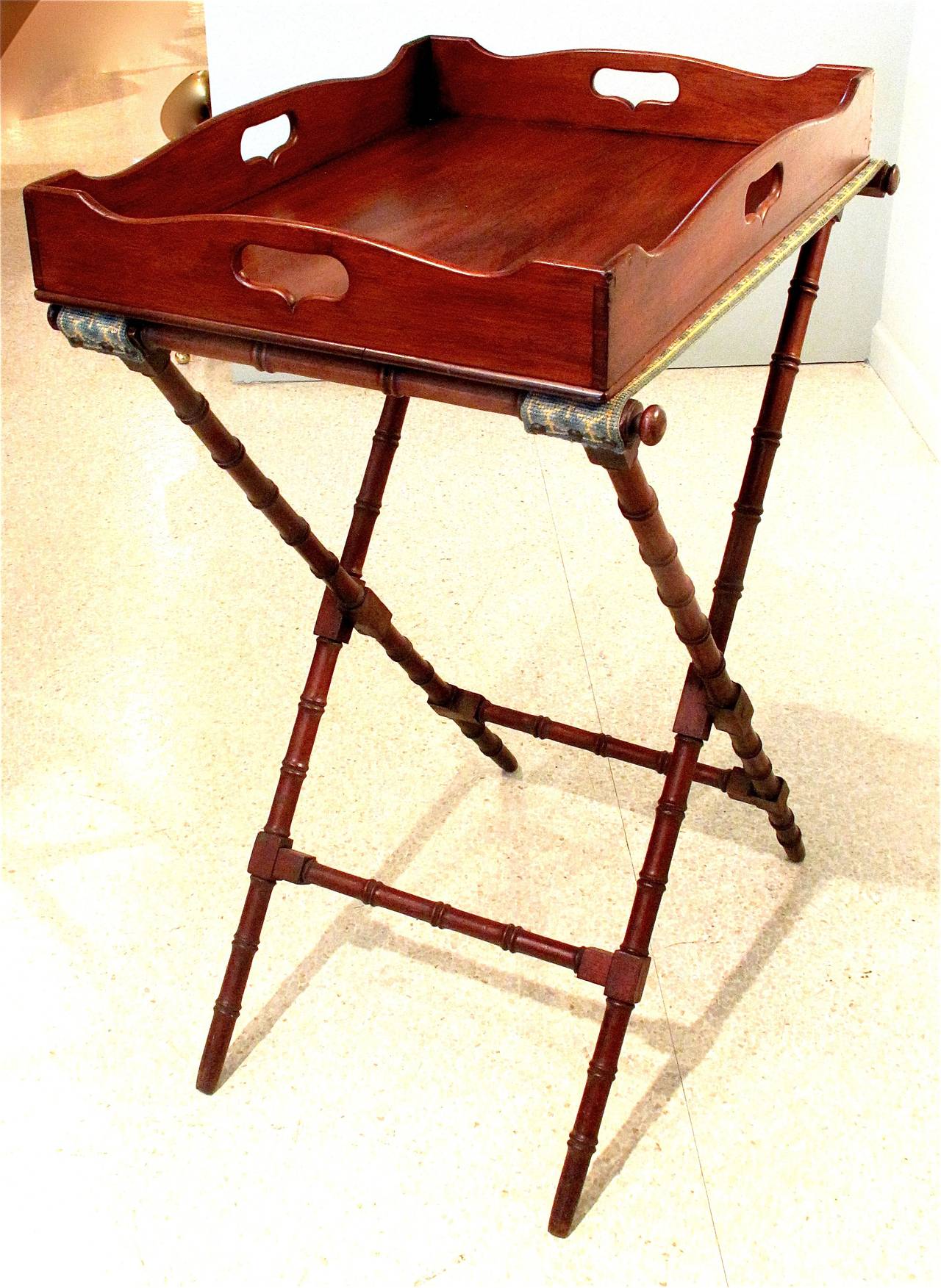 An early 19th century mahogany butler’s tray of rectangular form with a serpentine top line profile and shaped handles on all four sides, on a period bamboo turned legged folding stand. Needlepoint tray supports.
Tray alone H: 3 1/2 W: 24 D: 18