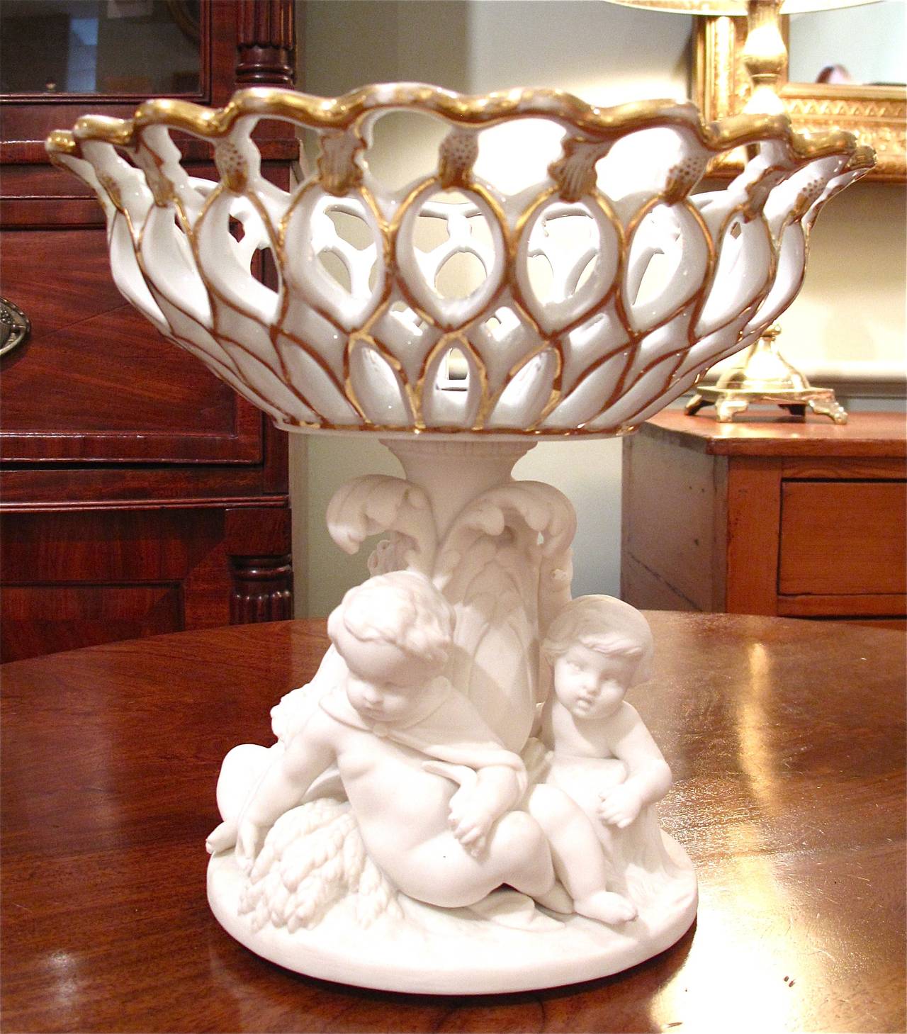 A very fine Minton compote with a Parianware pedestal base of frolicking putti supporting a glazed and parcel gilt basket. Stamped Minton and date marked 1865 on the bottom.