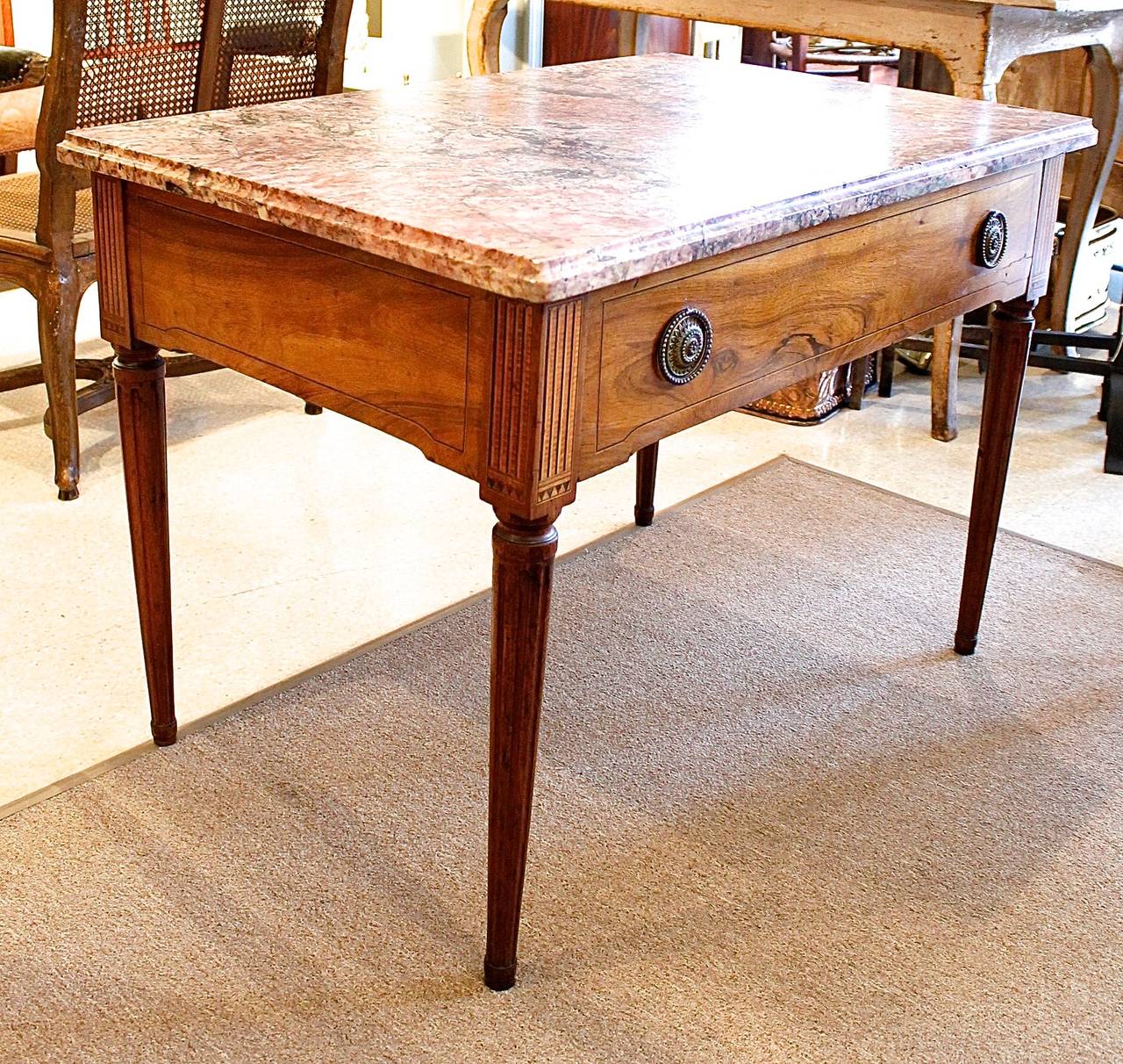 A stylish walnut center table with a marble top, finished on all four sides with inlay and slight shaping to the apron, the whole resting on tapered and fluted legs. Three sides have particularly nice marquetry at the stiles, simulating trompe