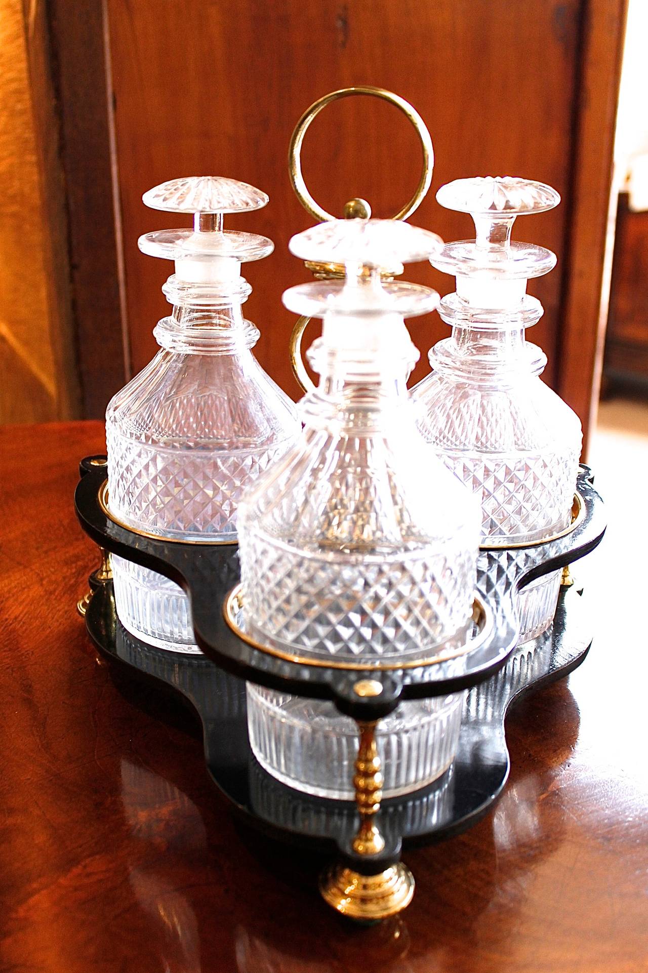 A fine set of three early 19th century matching blown and cut glass small liqueur decanters with double ring necks, fitted with a later Victorian custom made papier maché and brass tripodal caddy with a central handle. All in very good