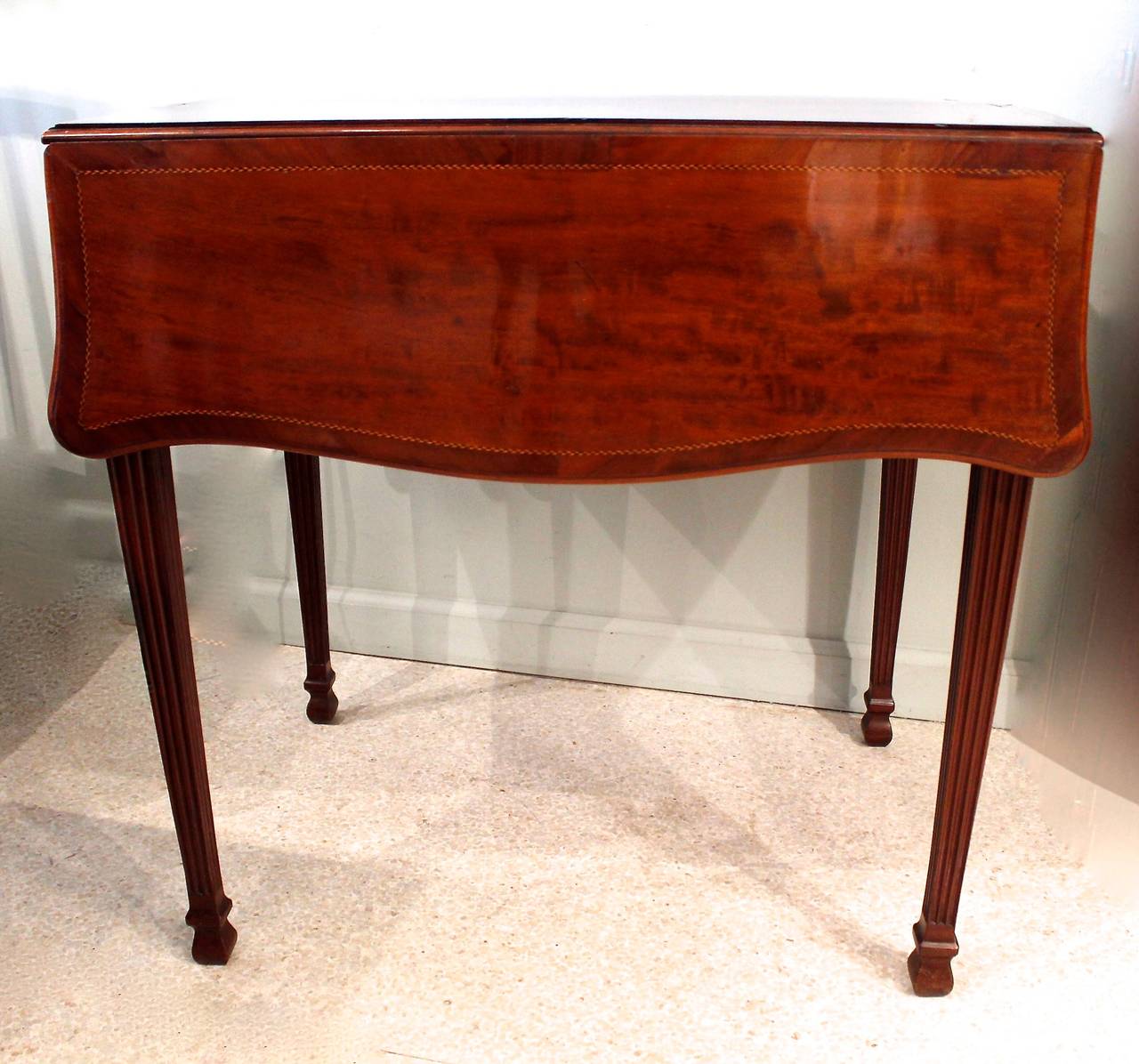 A small serpentine form Pembroke table, circa 1780s, of exceptional quality, with shaped leaves and tapered square fluted legs in the manner of Thomas Chippendale Jr. The top and drawers are cross banded and inlaid with a geometric herringbone