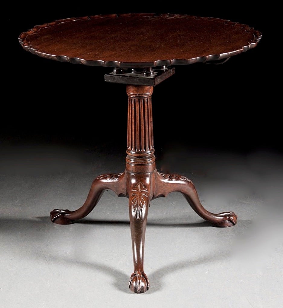 A very fine ca. 1760 English mahogany tilt top tea table, the pedestal base carved as a substantial fluted column resting on finely carved downswept legs with carved knees and terminating in elongated ball and claw feet. Birdcage retains original