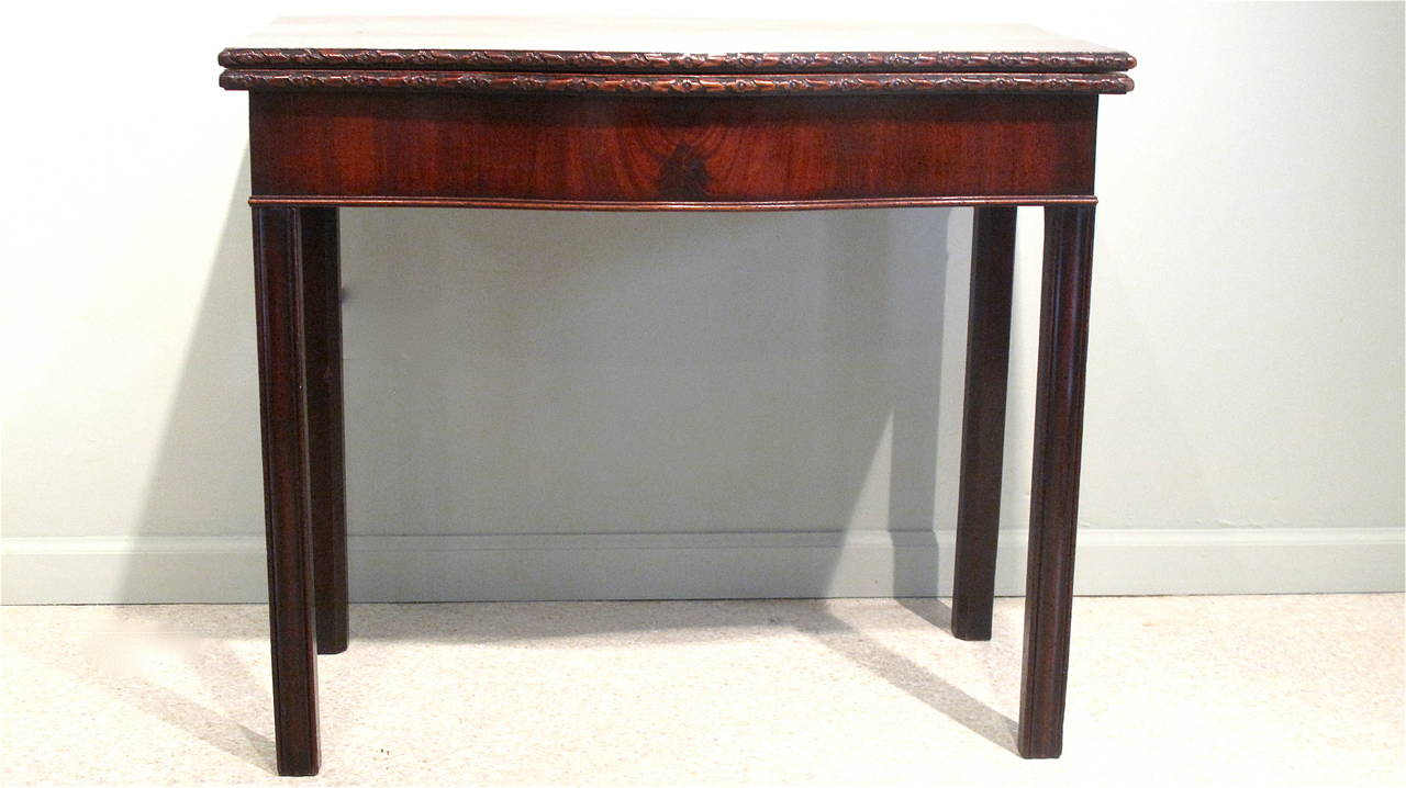 A flip top serpentine table, ca. 1780, with beautifully carved ribbon and rosette molding surrounding the rims, resting on straight Marlborough legs.