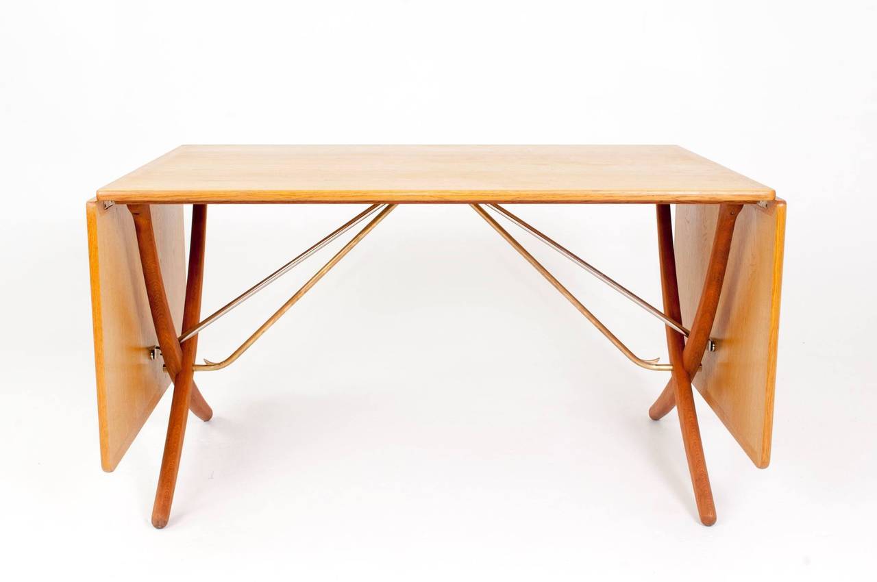 Hans J. Wegner.
Oak dining table with fold down leaves, mounted on frame with cross legs and brass stretchers.

Measuring 128 cm - 238 cm when fully extended. Depth 85 cm. Height 70 cm.