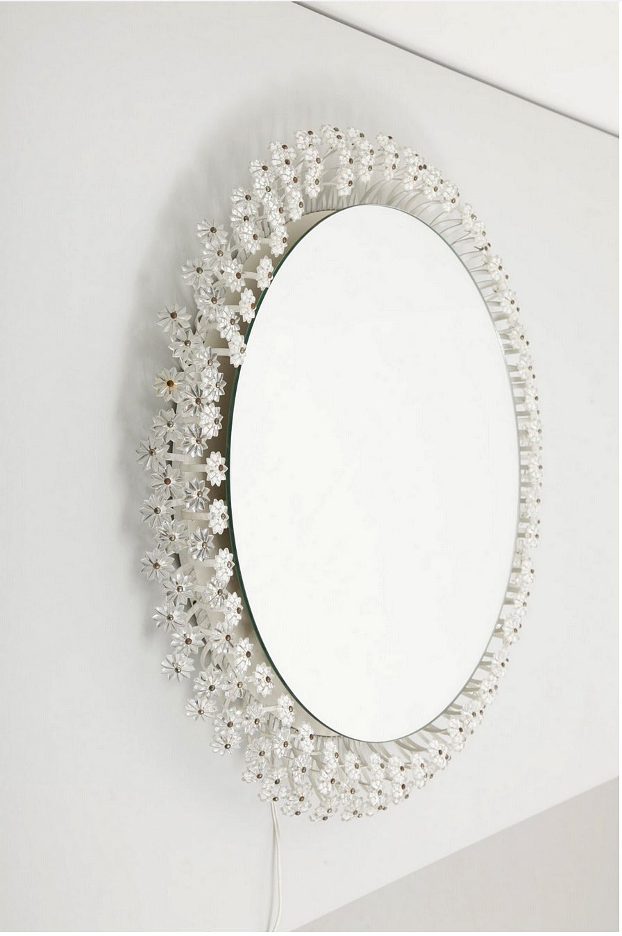 Ce miroir floral lumineux a été conçu par Emil Stejnar au début des années 1950 et fabriqué en Autriche par Rupert Nikoll. Elle présente un miroir rond, qui semble flotter, entouré d'un cadre en métal laqué blanc avec trois rangées de détails