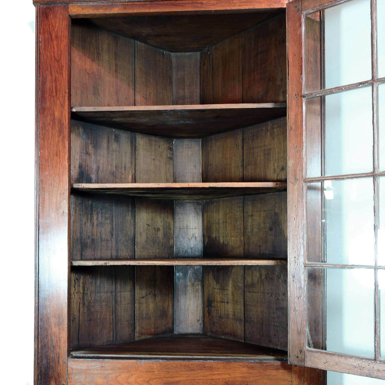 American mahogany (OAK/Walnut?) corner cupboard on bracket feet, late 18th or early 19th century. One-piece, comprised of 12 pane glass upper door with four interior shelves, over a single door cabinet concealing two additional storage shelves.