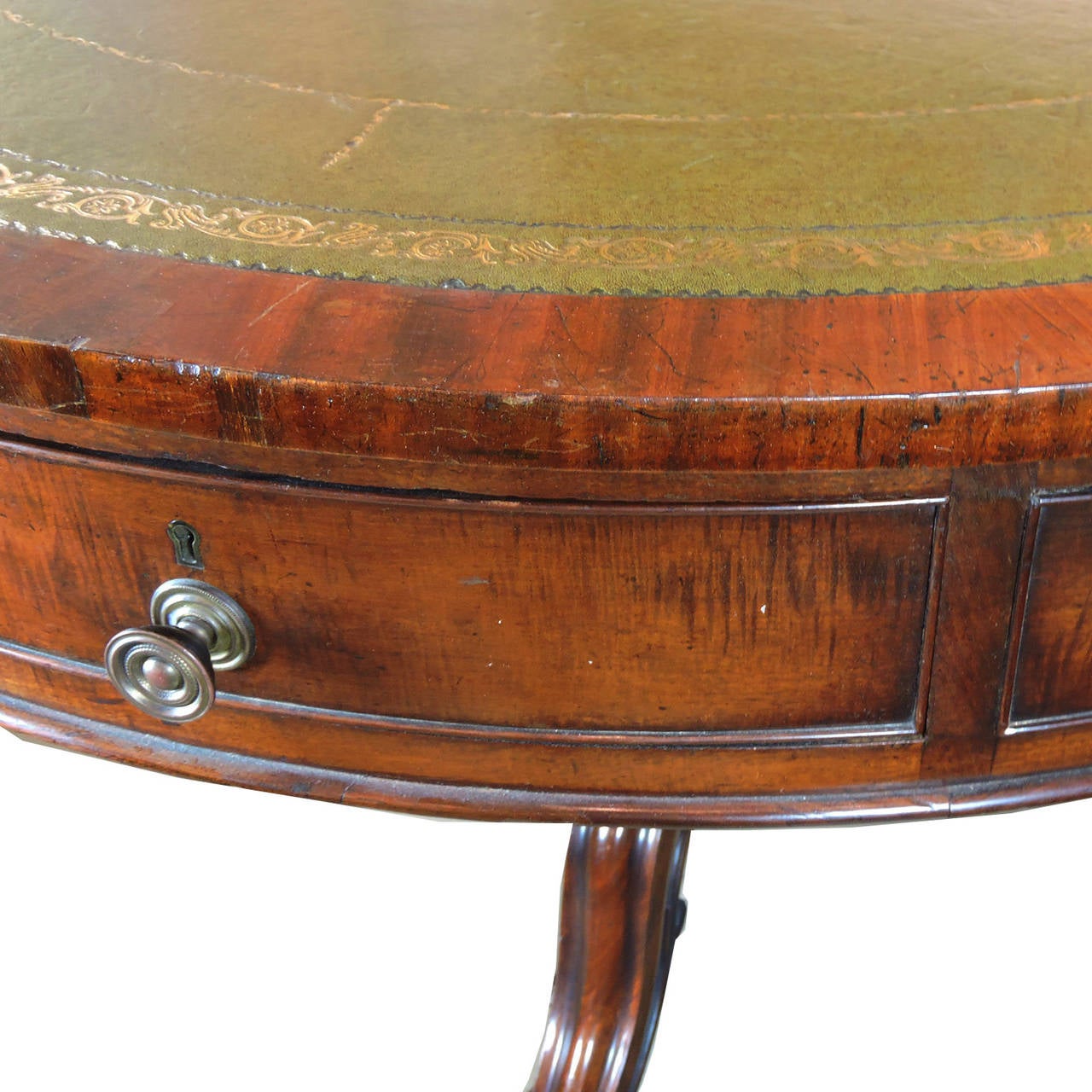19th century mahogany leather inset drum table, in the manner of Holland & Son, England. The gilt tooled green leather top over four drawers and four faux drawer, raised on a tripod leg base with scroll feet and casters. 
Measures: Height 31 1/4