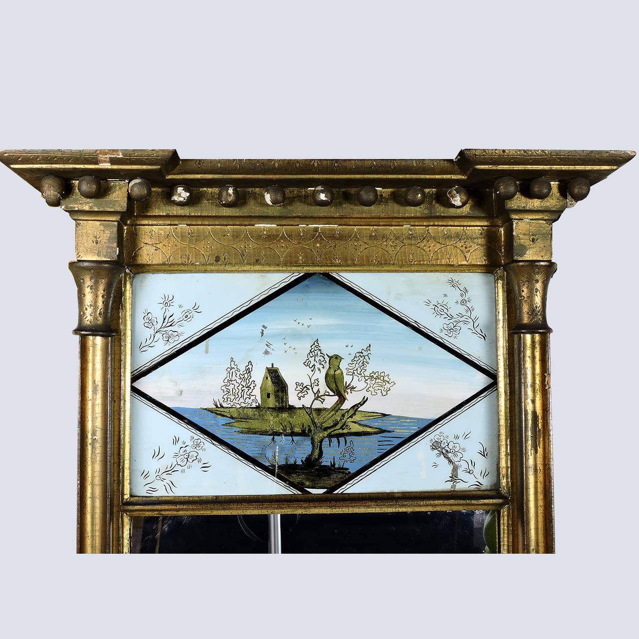 Federal carved giltwood églomisé wall mirror, circa 1800. The églomisé reverse paint gilt decoration of a bird in tree with a house on an island in the background. 
Dimensions: Height: 44 1/2 inches, width of cornice: 25 inches.