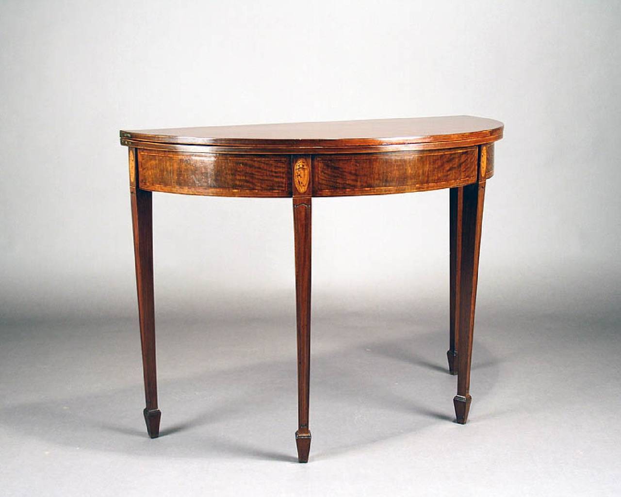 A fine quality George III inlaid mahogany tea / card table on tapering legs. The demilune solid mahogany top opens to an oval supported by the adjustable rear legs below which is a frieze boxwood strung with satinwood banding. Above each finely