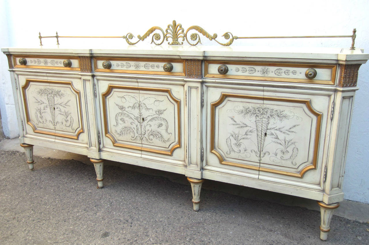 Fabulous Regency style galleried buffet cabinet made by Karges of Evansville, Indiana. Bronze anthemion and acanthas leaf gallery, ivory color with gold leaf trim with painted floral design on door and drawer fronts. 3 double door cabinets. 2 end