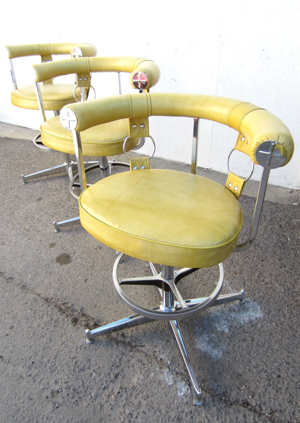 Tommi Parzinger style design bar stools with straps and rings in chrome and yellow vinyl by Daystrom Furniture of Boston. Each swivel with adjustable foot rest height. 
Each is dated April 13, 1978 on bottoms