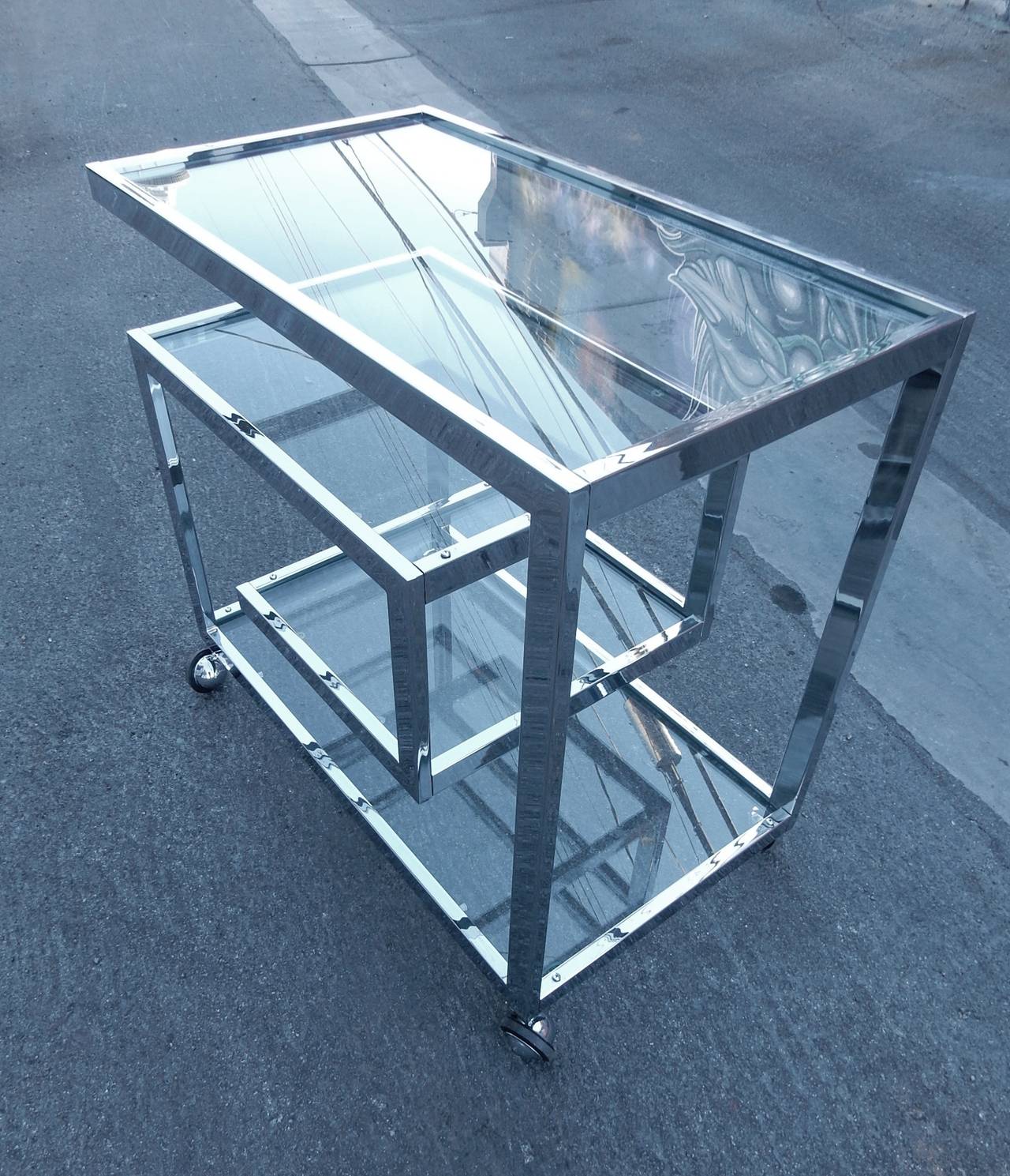 Spectacular example of a Milo Baughman design with flat bar chrome, Greek key design.
This bar cart has 4 glass shelves and smooth rolling casters. 
Excellent condition!
