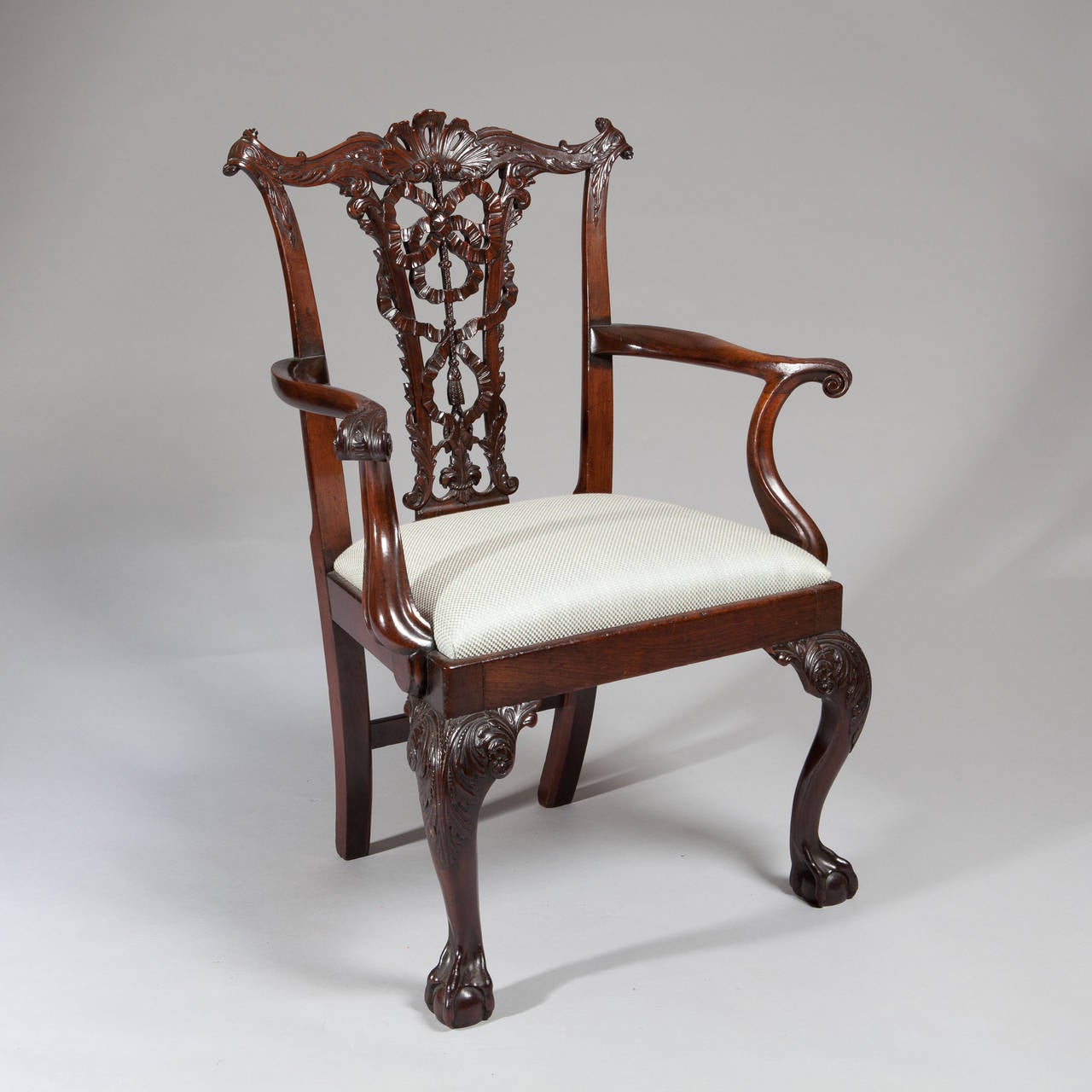 A pair of 19th century Chippendale armchairs, the open carved splats with intertwined ribbons and foliage, the top rails with acanthus leaves and scrolls, the exaggerated arms sweeping forward with great extravagance to scrolled ends, the chairs