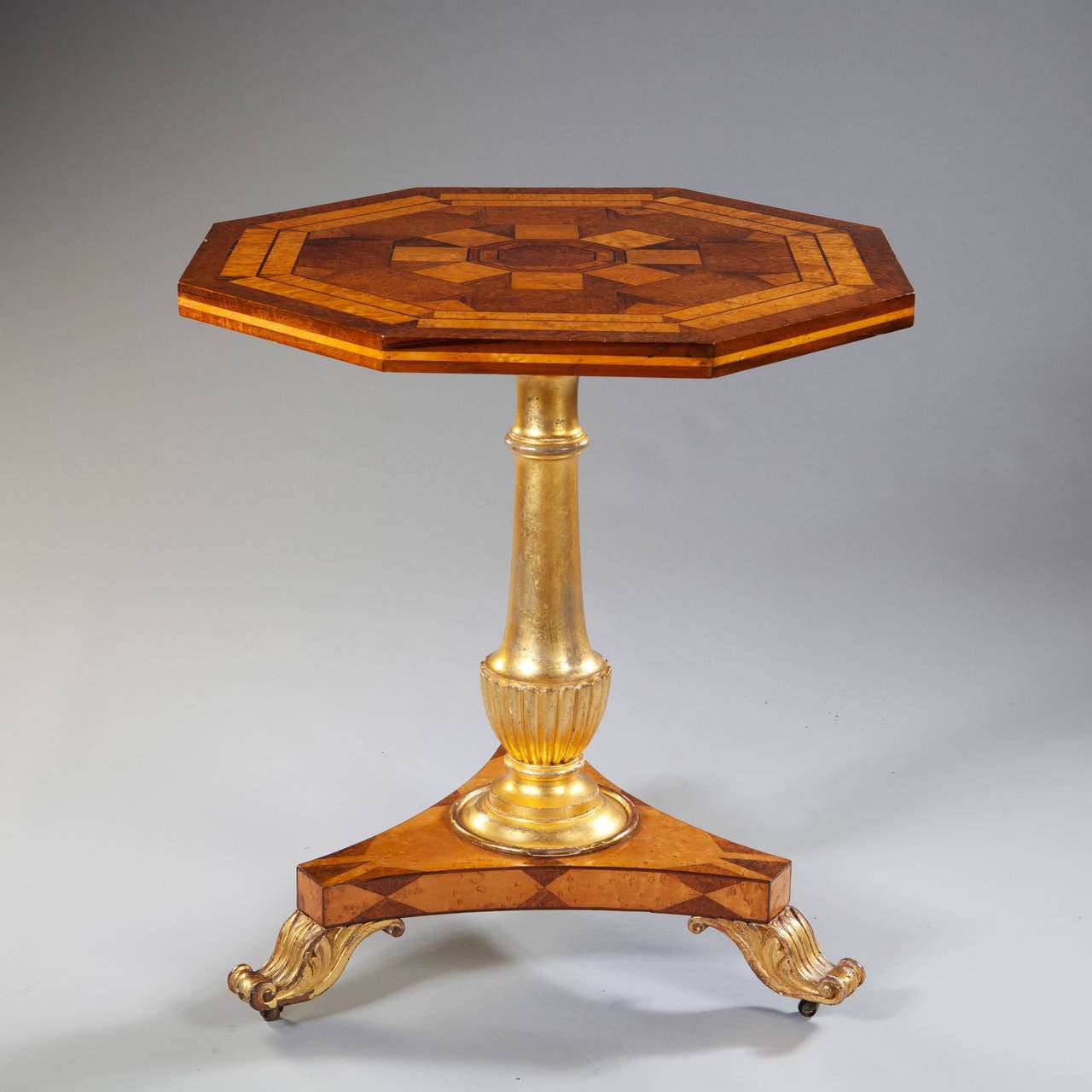 A very fine marquetry tilt top octagonal table, the geometric marquetry top inlaid with fine veneers of birds eye maple, walnut, mahogany and yew wood, raised on a gilt column and standing on a three sided concave base with marquetry lozenges and