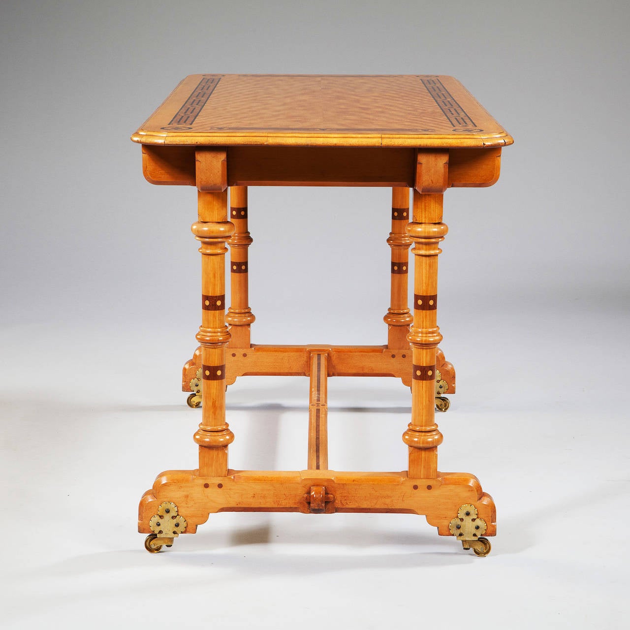 Une écriture Arts and Crafts en bois de satin richement incrustée d'ornements feuillus stylisés et de bandes transversales multicouches. La table repose sur des colonnes tournées reliées par une civière soutenue par une volute, et se termine par des