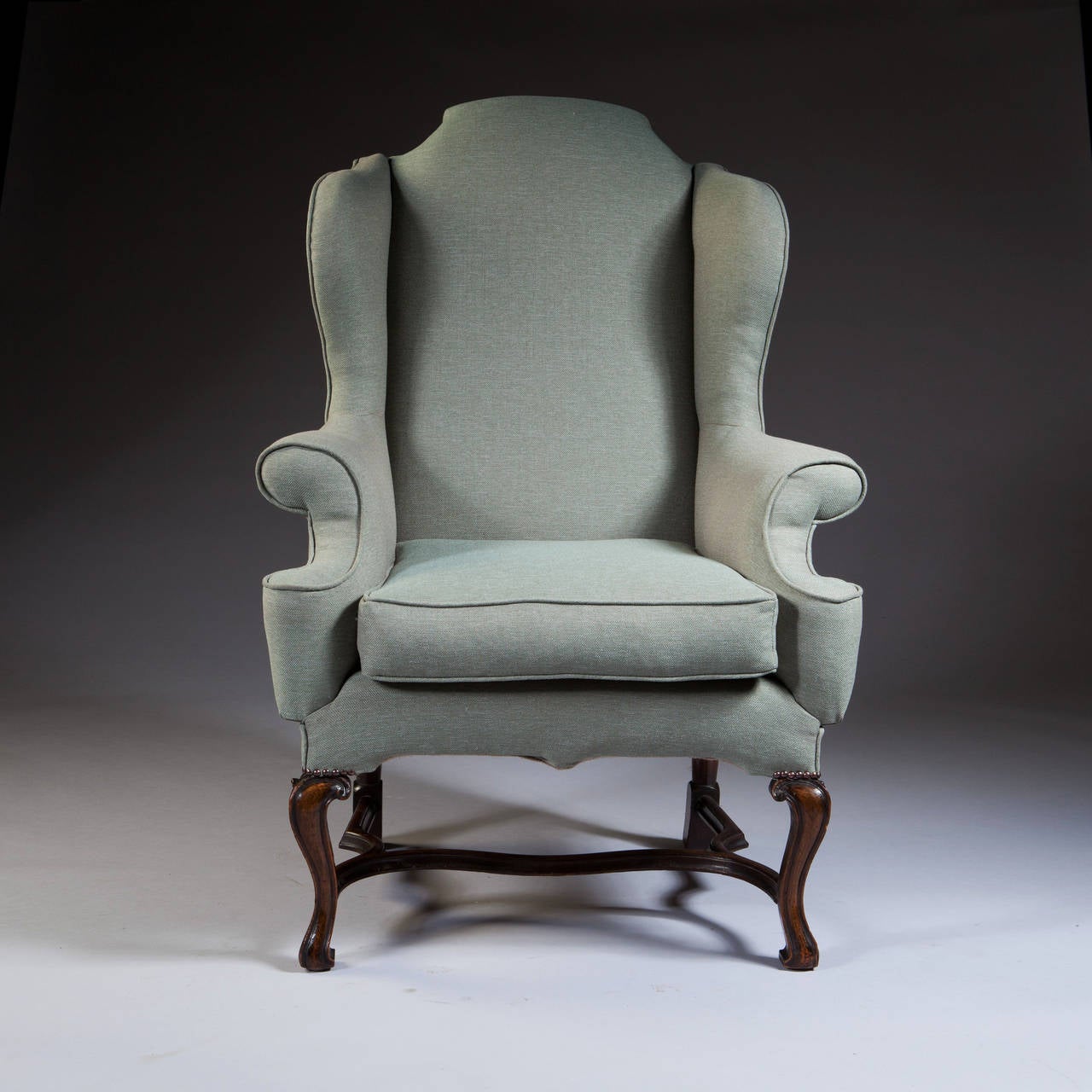 An elegant and good sized George I style wing chair, raised on cabriole legs with scroll toes and an interesting carved stretcher.