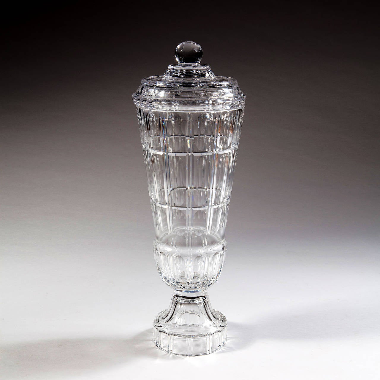 A very large scale Val Saint Lambert clear glass vase and cover. The sides and cover are cut with bold flutes, gashes and varying scale ovals. The cover terminates in a large ball finial. The base is a strongly fluted and facetted.