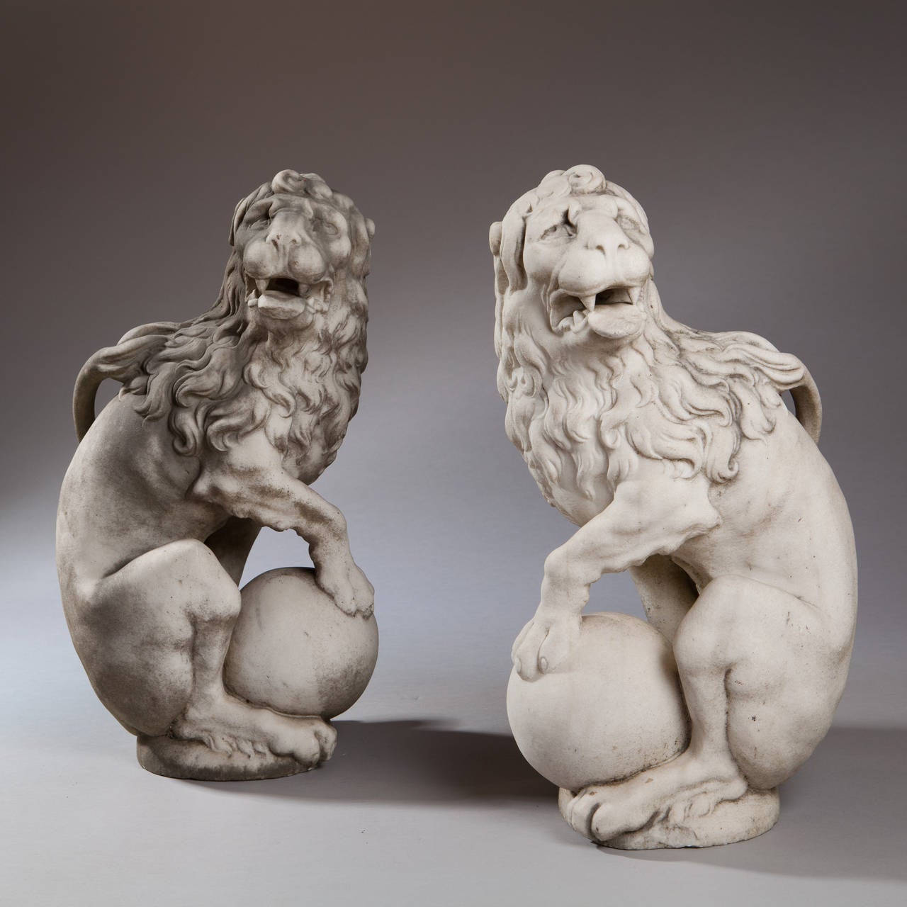 A exceptional pair of mid 17th century carved white marble seated lions, each with one foot raised steadying a ball.