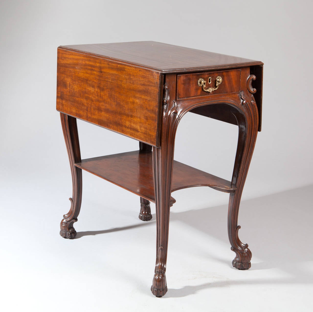 The rectangular twin-flap top above a mahogany-lined frieze drawer, the reverse with a simulated drawer, on carved cabriole legs headed by foliate carving, with a concave-sided shallow-galleried undertier inswept at the front, on elaborate carved