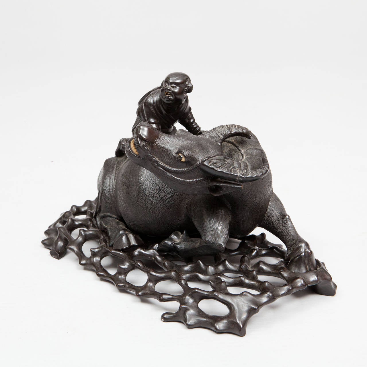 ​A very fine example of a Chinese 19th century carved recumbent water buffalo with a boy seated on his back. The well-carved Chinese hardwood is of an even dark tone with very fine carving, raised on its original hardwood pierced base representing