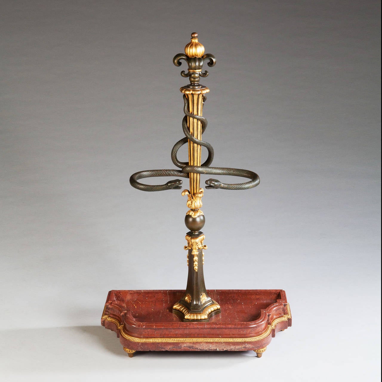 An exceptional parcel-gilt bronze stick stand, the shaped red marble base supporting a fine bronze and parcel-gilt fluted and mounted column with a pair of finely cast entwined snakes as the rests. The whole standing of gilt feet with a running