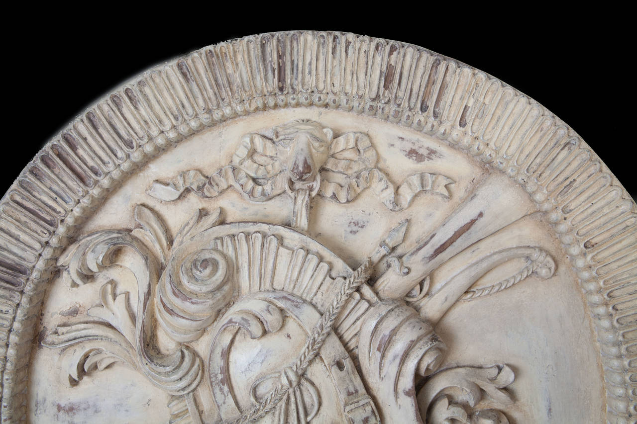 A pair of late 19th century carved and stone painted circular martial trophy roundels, each with a boldly carved fluted border. The trophies suspended from the mouths of lions.